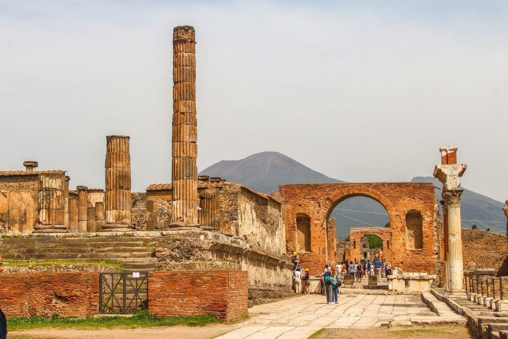 The brightly lit up forum at Pompeii, lots of tall roman columns, underneath the golden sunlight.