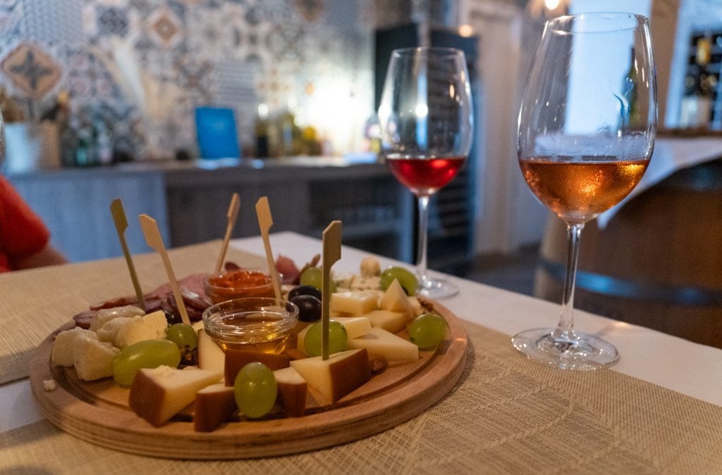 A hearty plate of charcuterie, cheeses, nuts, and grapes, next to two glasses of rose wine.