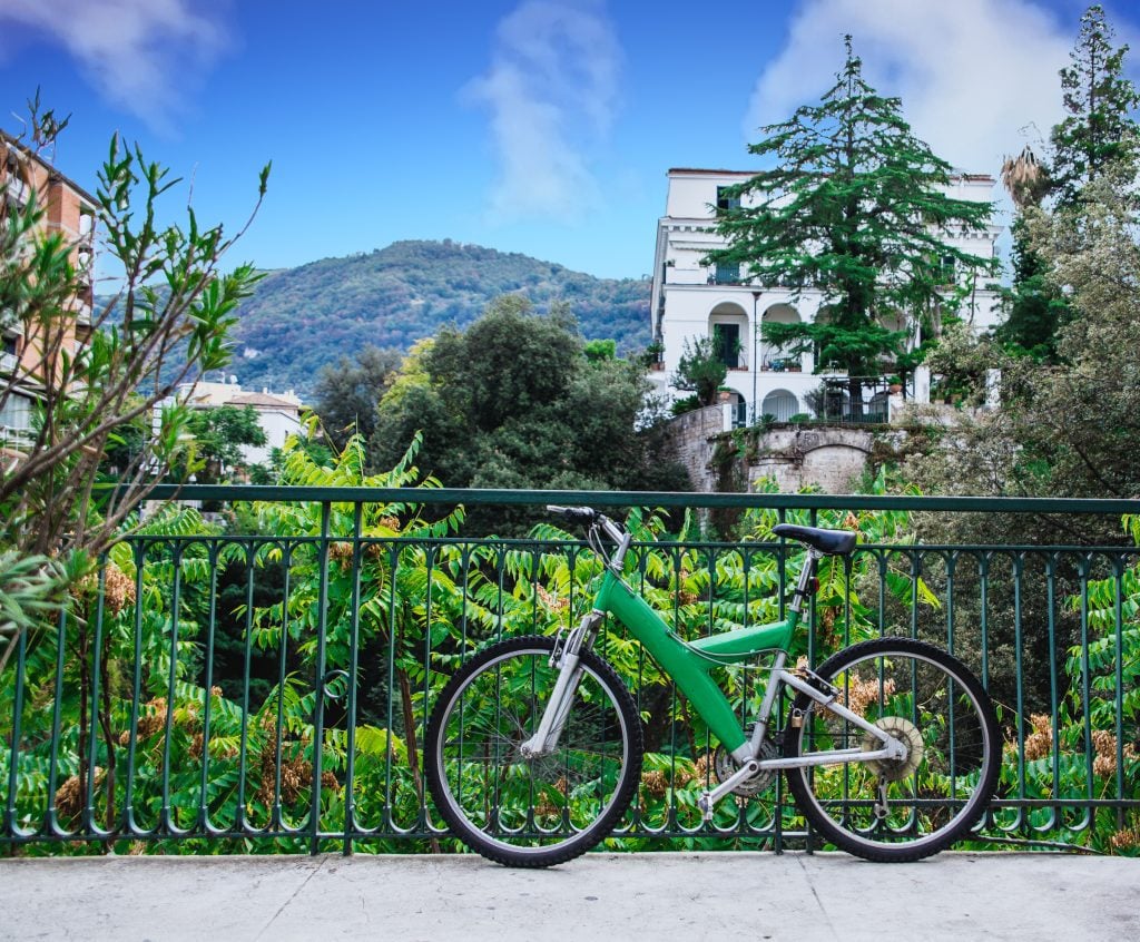 A green bicycle parked in front of a garden in Sorrento, a big white villa in the background.