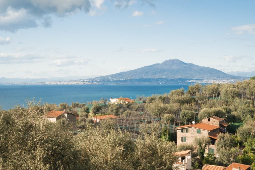 A view of Mount Vesuvius in the distance, with rolling green hills and farmhouses in the foreground.
