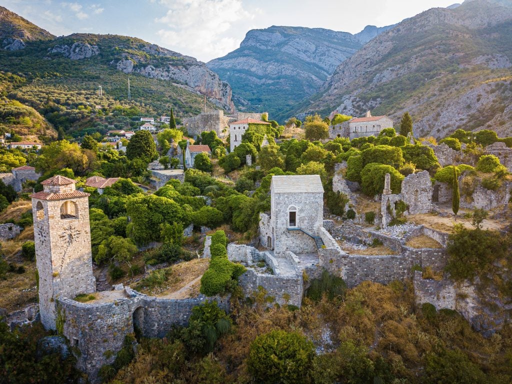An ancient city of rocky walls set against a mountainous backdrop.