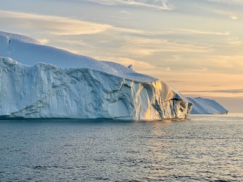 A huge iceberg lit up in pale yellow sunset light.