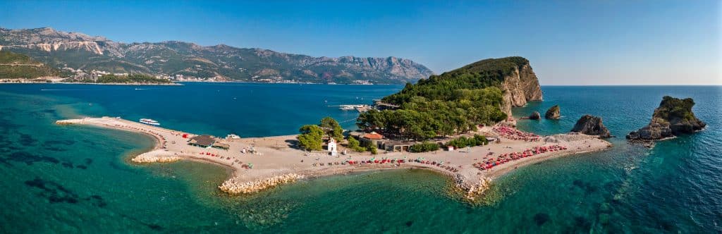 A small island with bright green cliffs and lots of sandy beaches, close to shore in Montenegro.