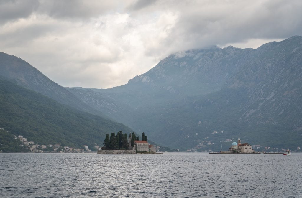 Two tiny islands in the still bay on a gray, cloudy day.