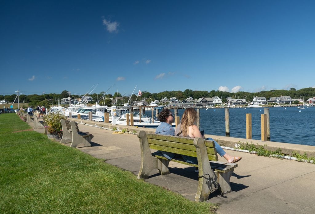 Two people sitting on a park bench in Martha's Vineyard, on the edge of the water.