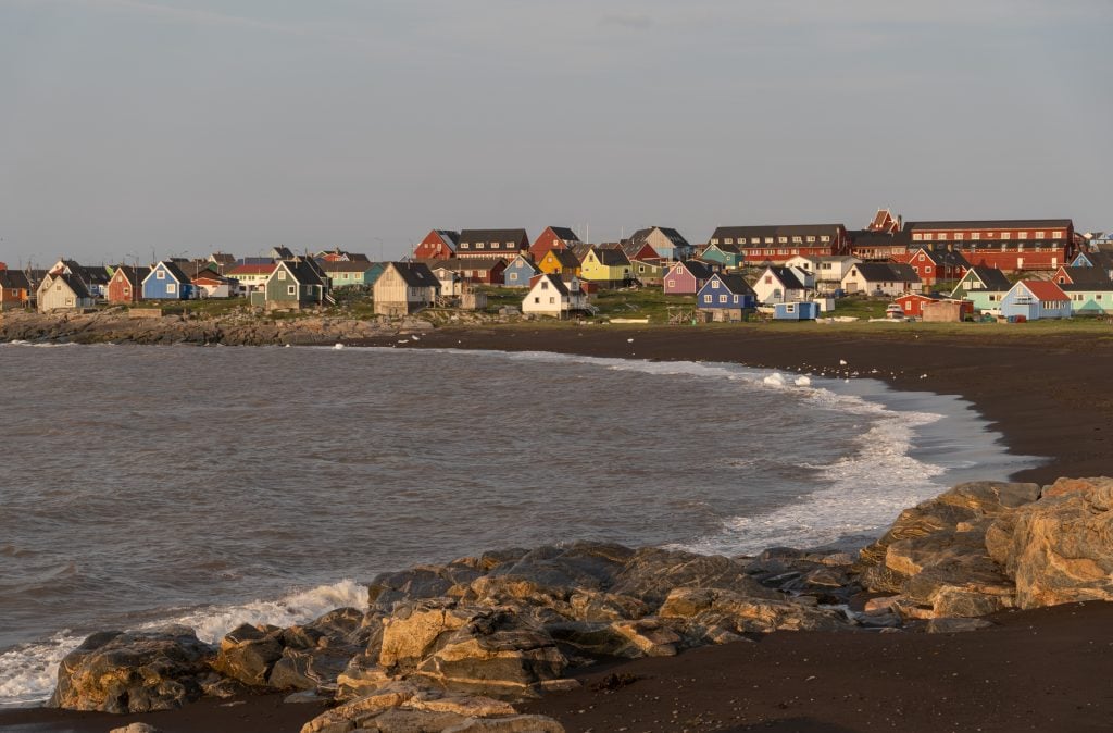 A black sand beach with brightly painted home curving around it.