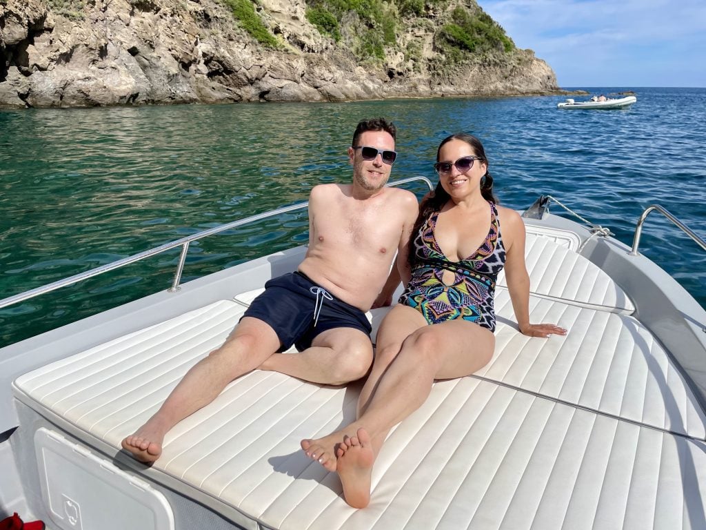 Kate and Charlie in bathing suits, sitting on the bow of a boat in front of some clear green water in Ischia.
