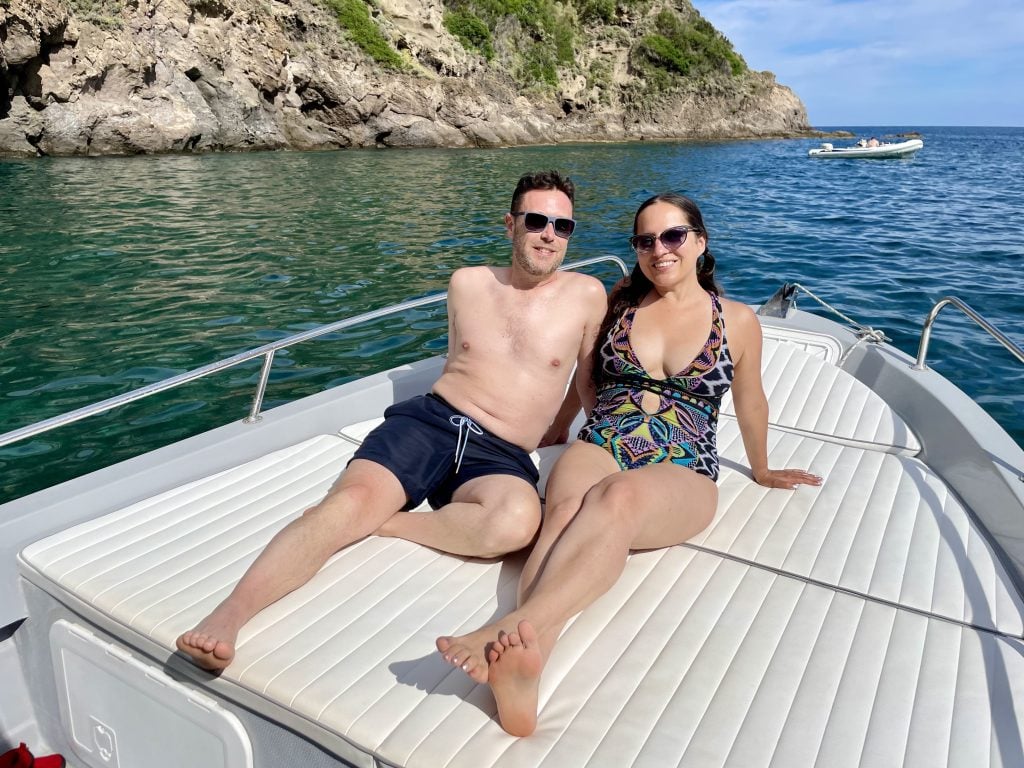 Kate and Charlie in bathing suits, sitting on the bow of a boat in front of some clear green water in Ischia.