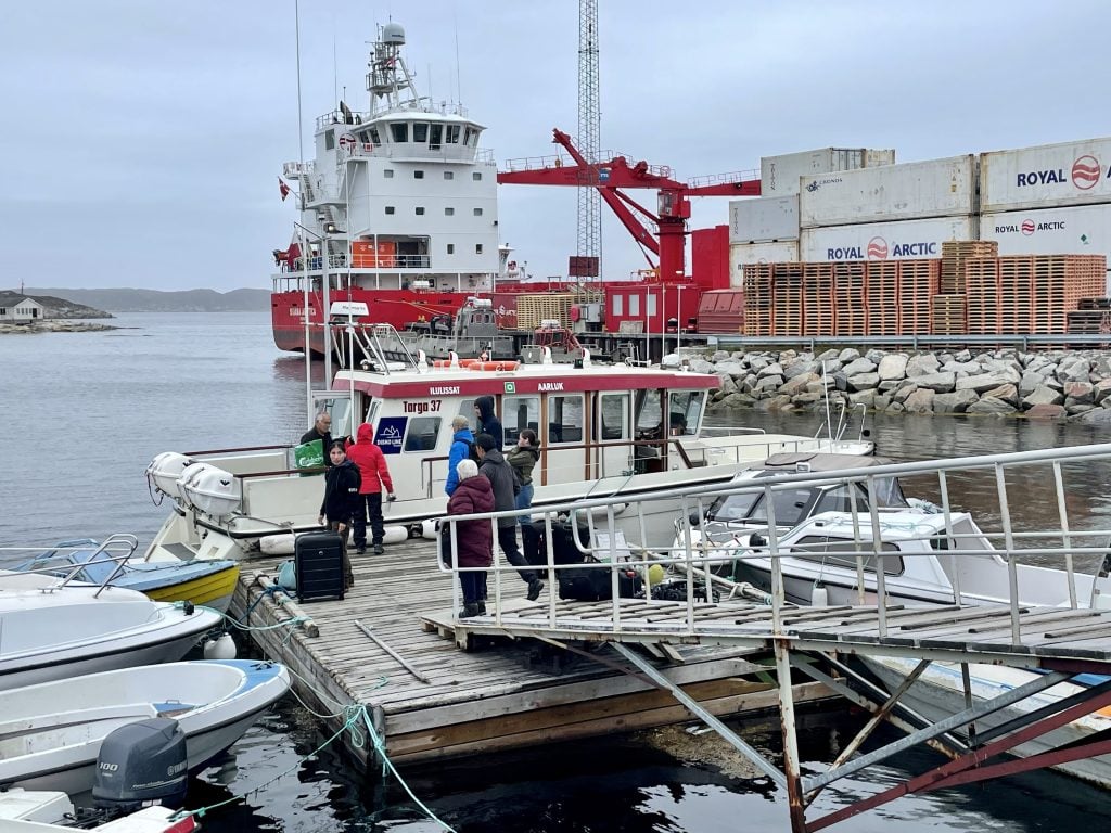 A small wooden boat at the end of a makeshift pier in Aasiaat, Greenland. Passengers getting off and on.