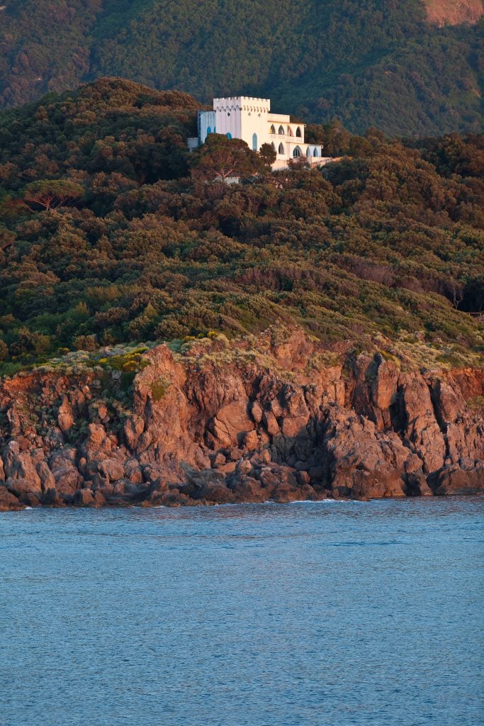 A white villa standing in the middle of a forest, on top of a cliff tumbling into the sea.
