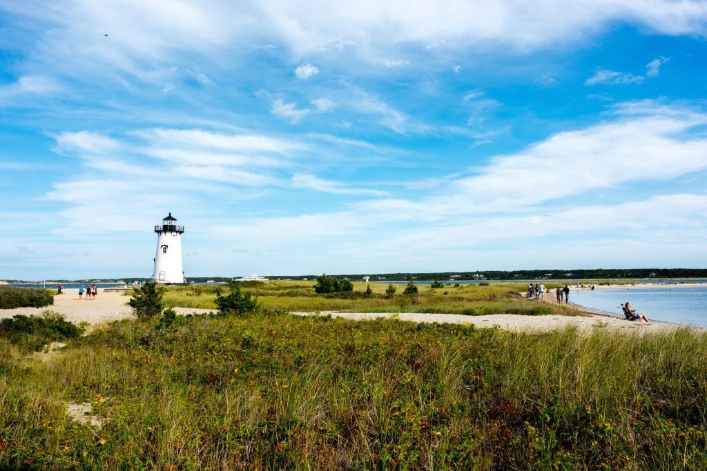 A lighthouse on a narrow spit of sand, some of it covered with grass.