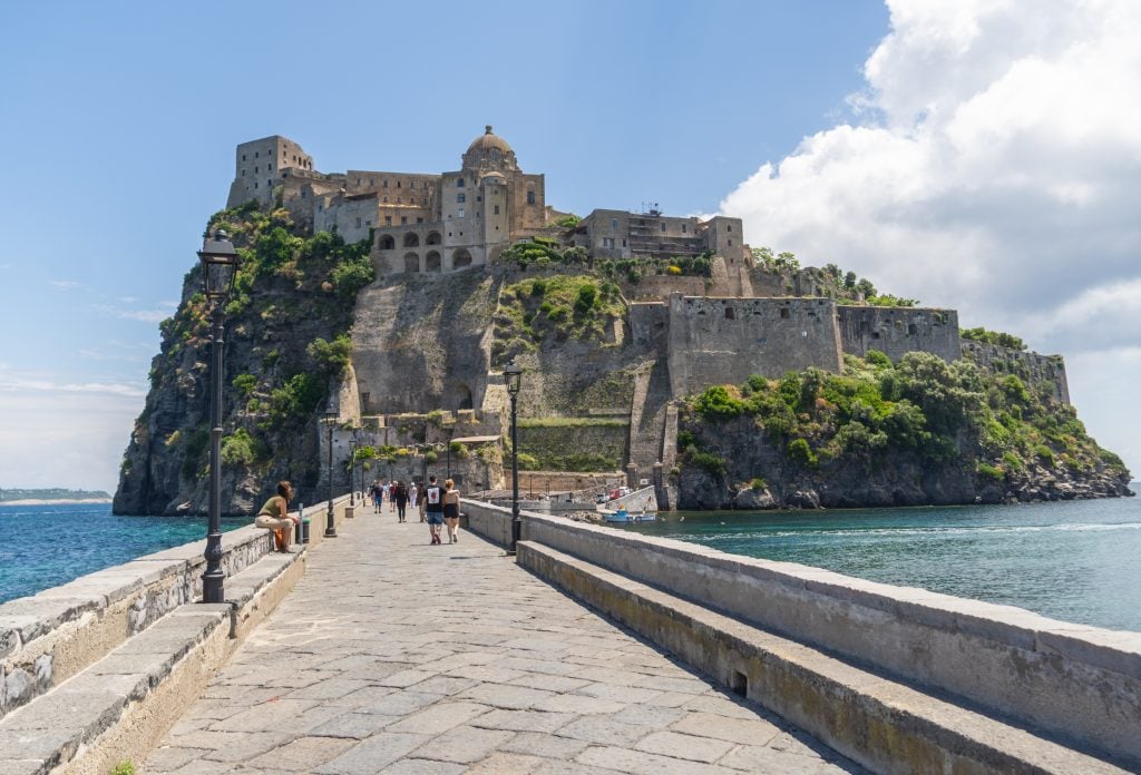 A stone pathway across the water leading to a small island topped with a castle.