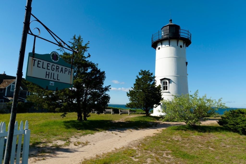 A big white lighthouse next to an old-fashioned metal sign reading "Telegraph Hill."