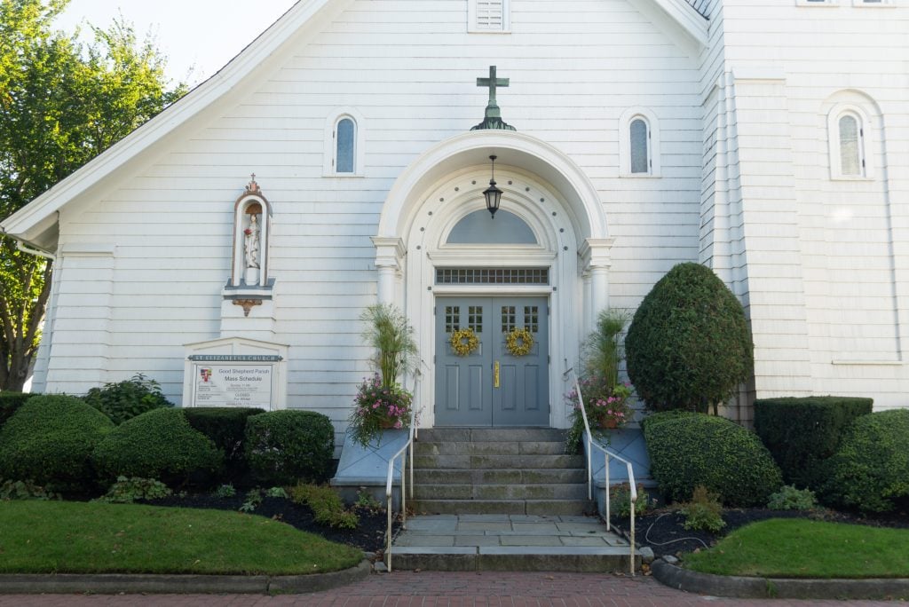 A clean, white, modern church with a sloping roof in Edgartown. The front door is a soft shade of blue.
