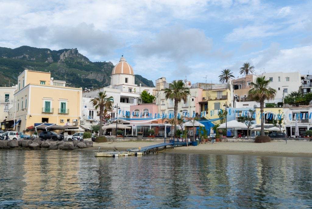 A small town perched on a beach in Ischia. There's a church with a bright orange and yellow dome.