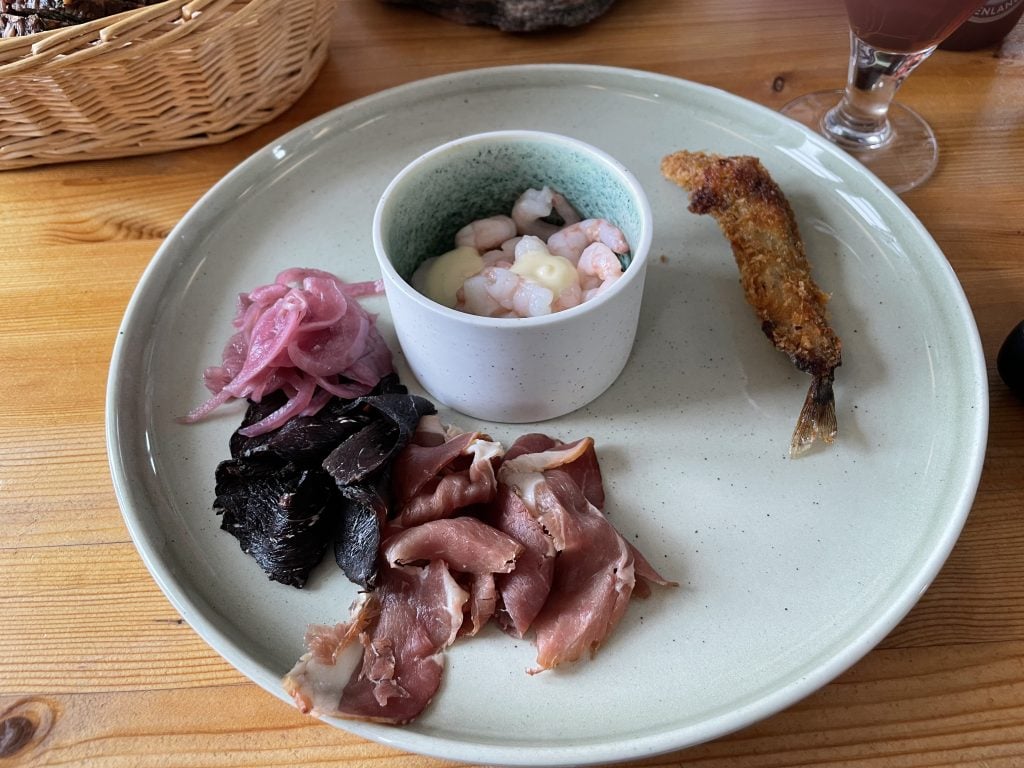 A plate covered with sparse pieces of cured lamb, cured whale meat, a small fried fish, pickled red onions, and a small dish filled with tiny shrimp. Not very appetizing.
