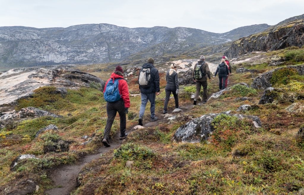 Five people hiking along a path surrounded by a craggy green landscape.