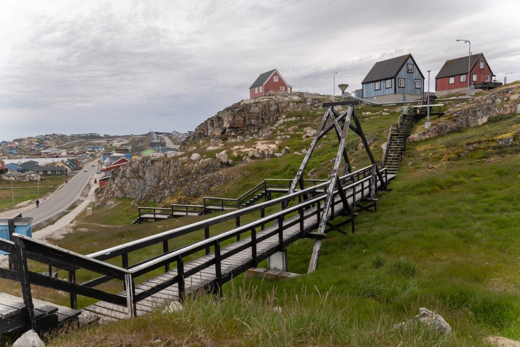 A small hill with cottages perched on the top and a wooden pathway with railings leading down the steep hillside.