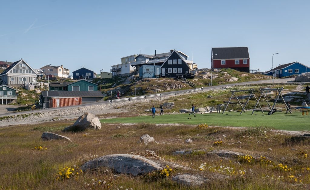 Kids playing on a football pitch in Greenland, surrounded by colorful wooden houses.