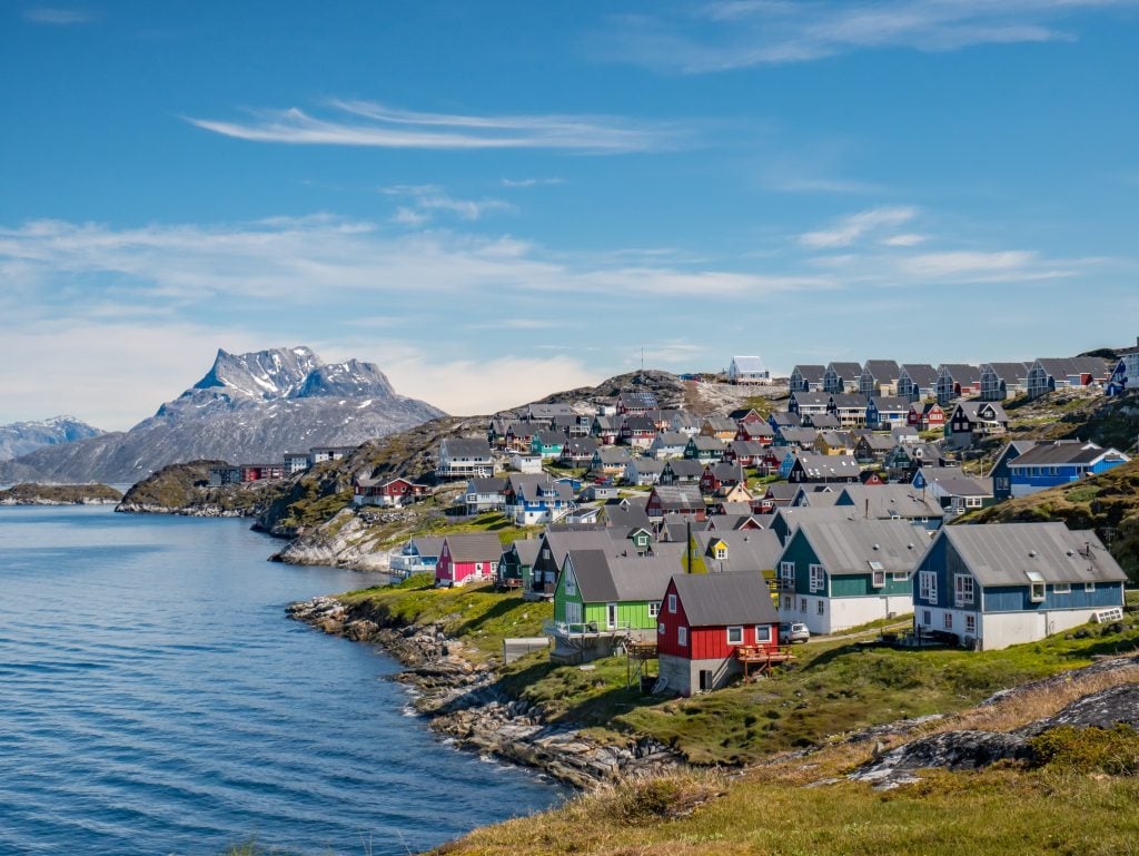 Brightly colored cottages perched on the coastline in Nuuk, Greenland, a mountain in the distance.