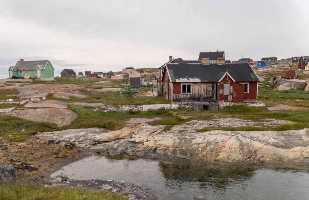 Oqaatsut, a small town in Greenland with rundown cottages scattered on rocky terrain.