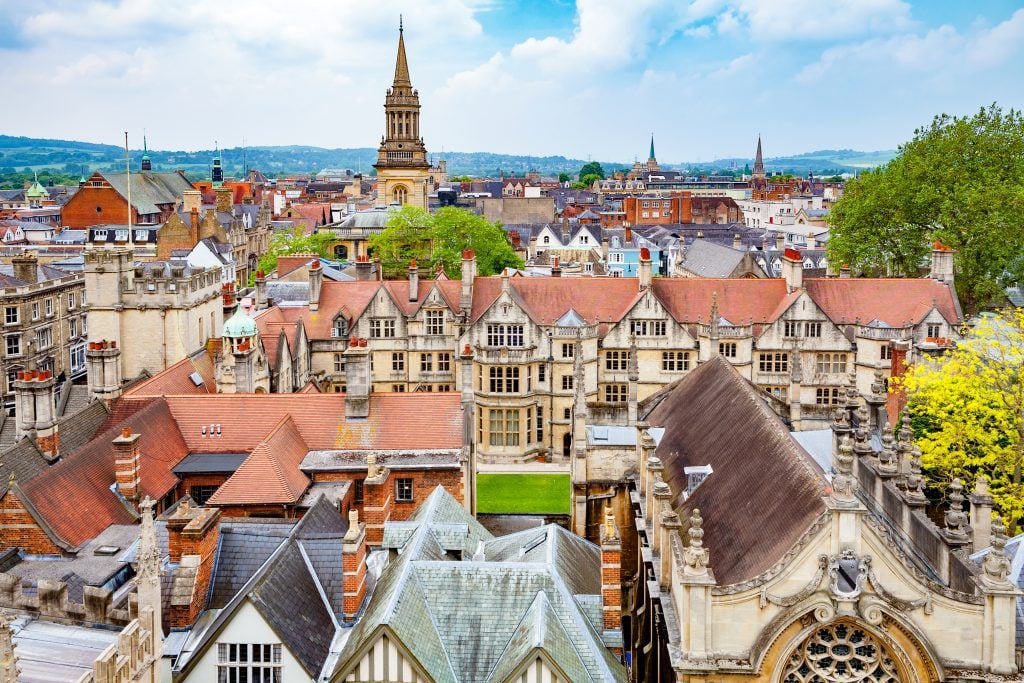 Oxford England, with layers of gothic church steeples and stone buildings, underneath a partly cloudy sky.