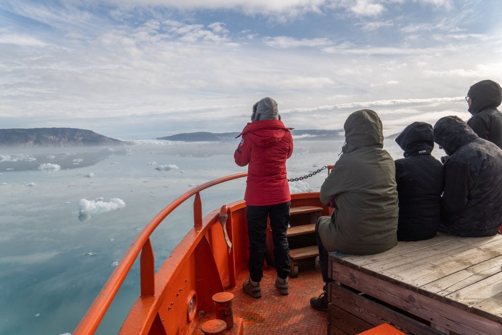 People standing on the bow of a bright red boat, taking photos of a glacier in the distance.