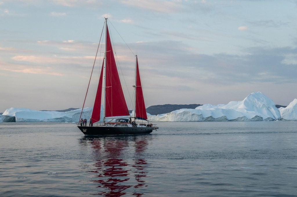 A sailboat with blood-red sails sailing among the calm blue-gray landscape of the ice fjord.