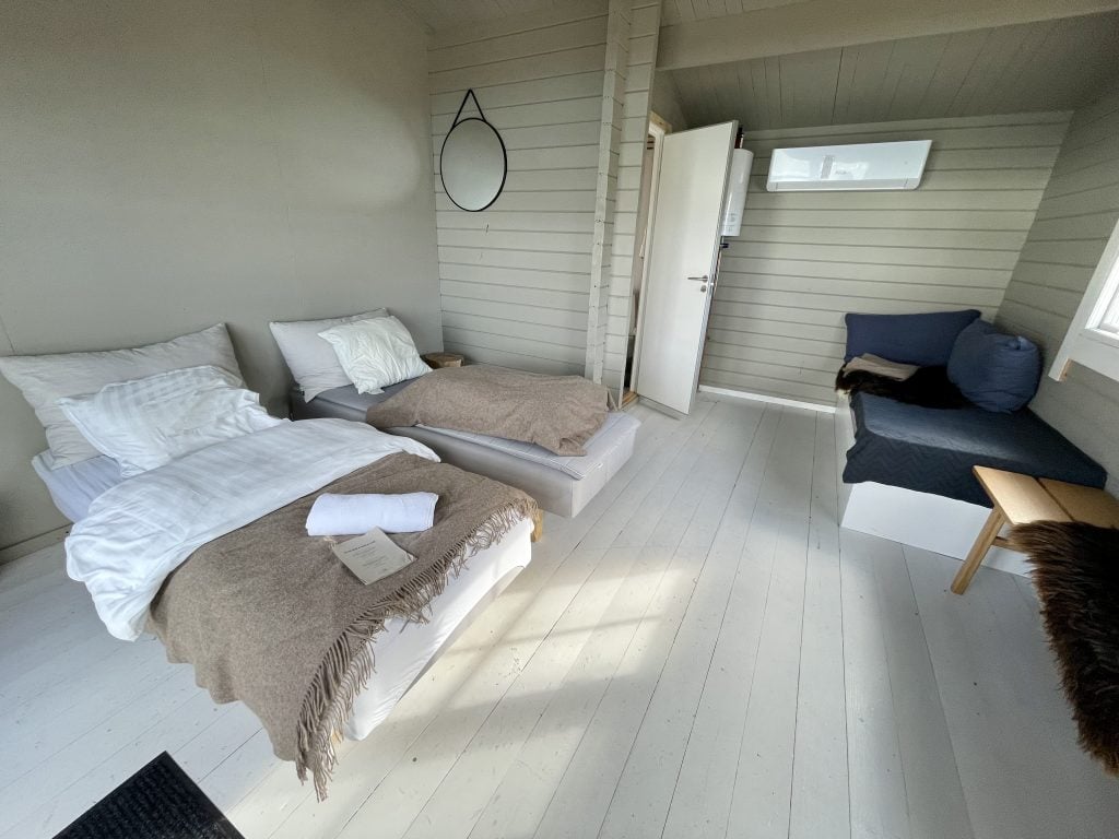 The inside of a hut at Glacier Camp Eqi: Two twin beds covered with heavy blankets, a day bed, a hanging round mirror, and a little bathroom nook in the back.