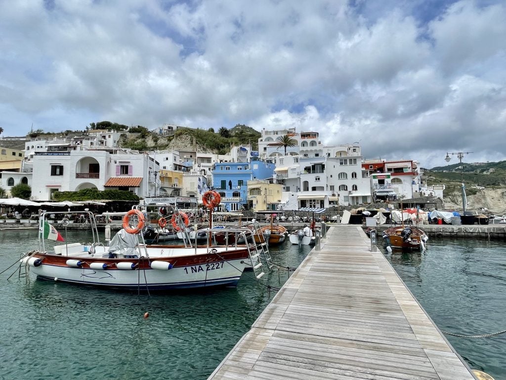 The view walking on a wooden dock into a small colorful Italian village, wooden boats in the water.