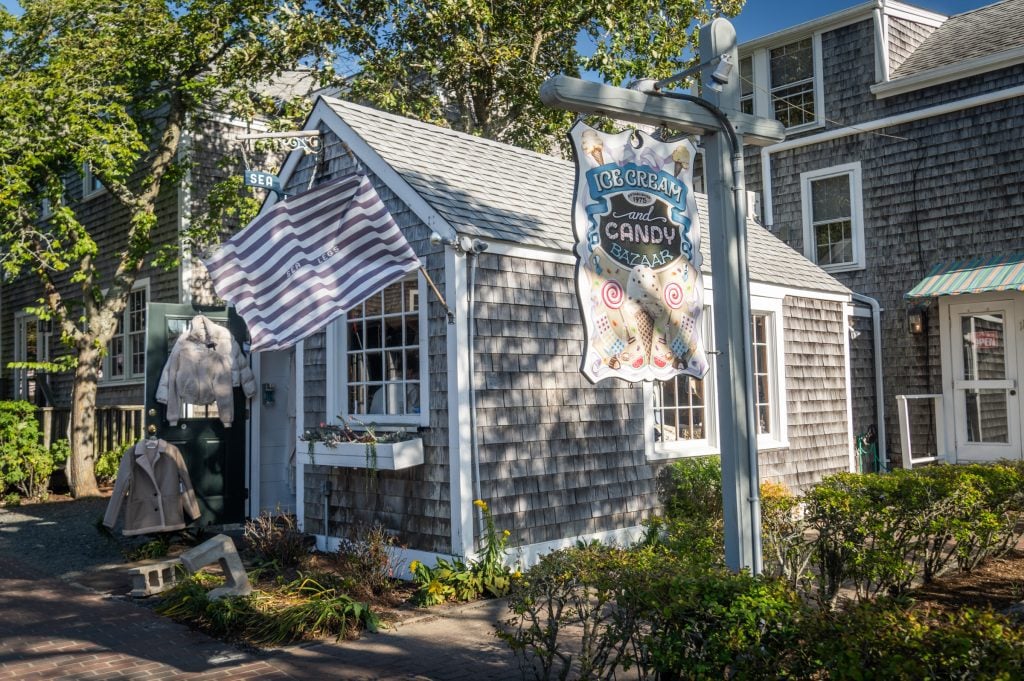 A small clapboard house with a sign reading Ice Cream and Candy Bazaar and a faded American flag hanging out front.