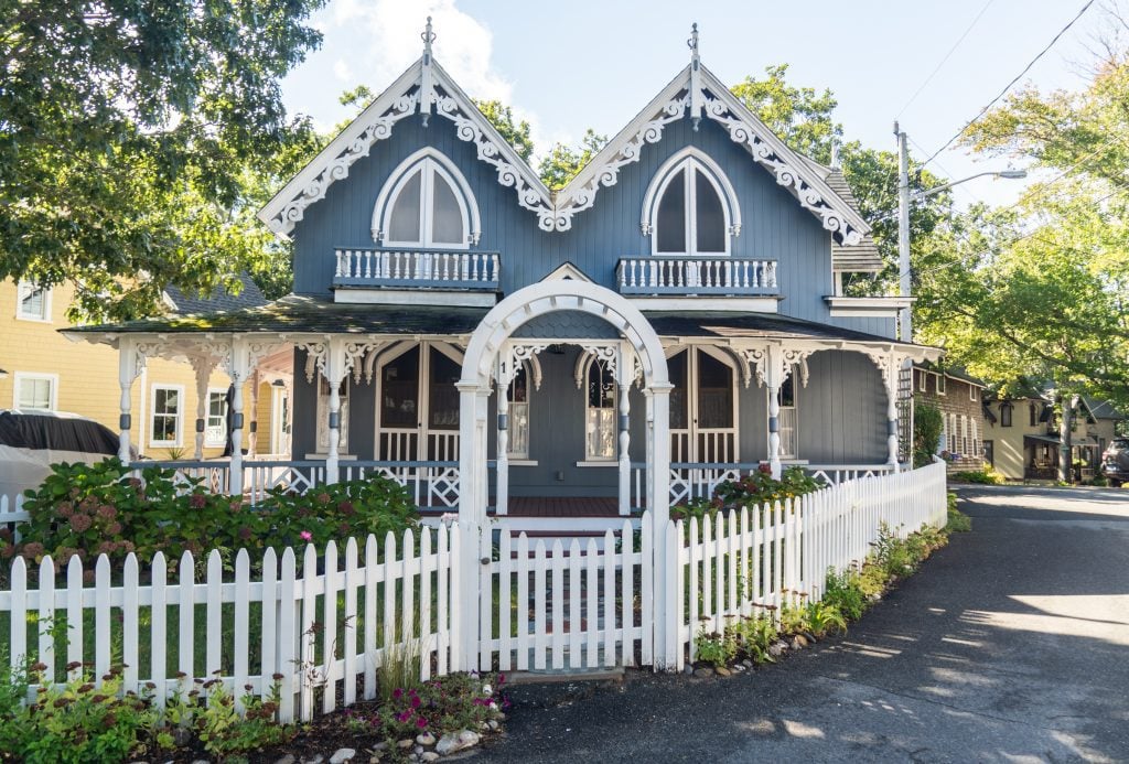 An elaborate slate blue Victorian house with a white picket fence and lots of white wooden cutouts as decoration.