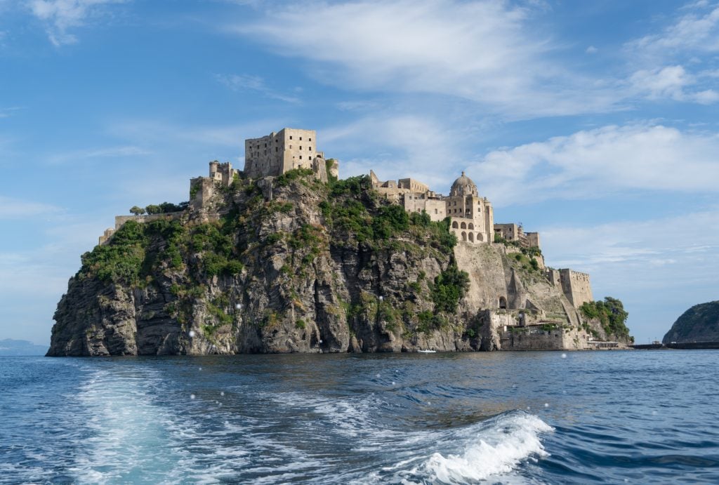 The rocky island topped with the castle, as seen from the sea, looking as if it's surrounded by water on all sides.