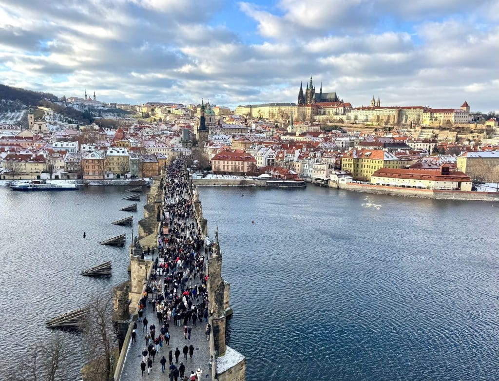 Prague Castle sitting on a hill, with the Charles Bridge leading to it, all underneath a faint dusting of snow.