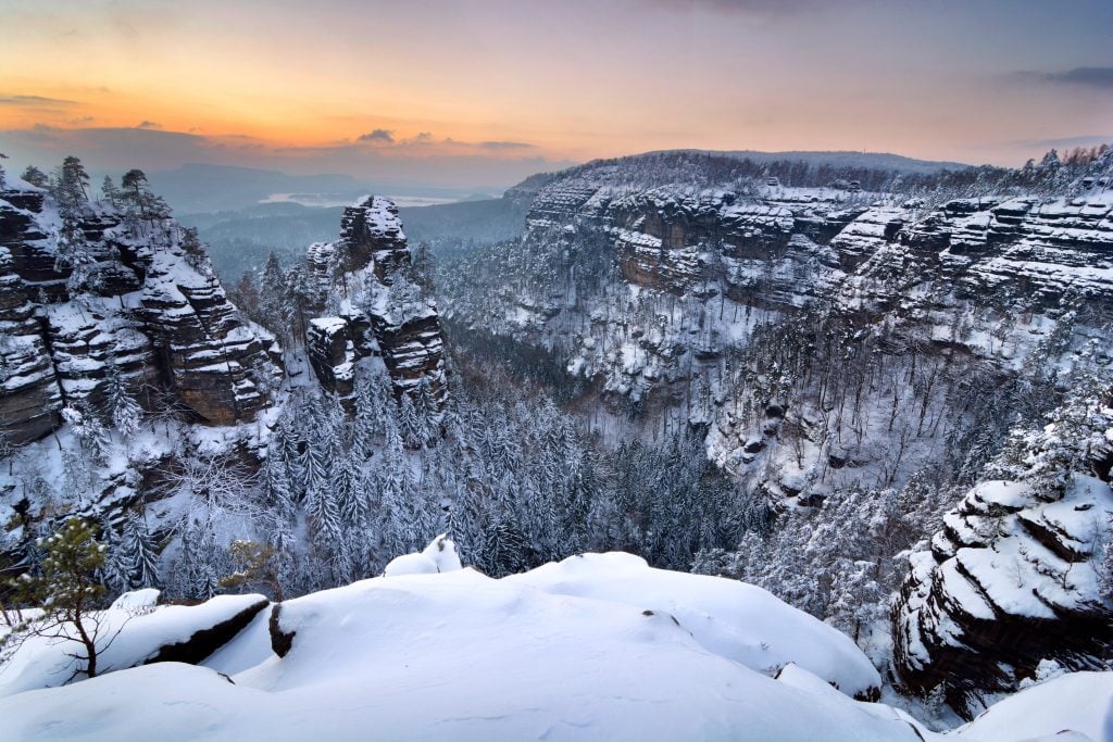 A snowy forest surrounded by a mountainous landscape.