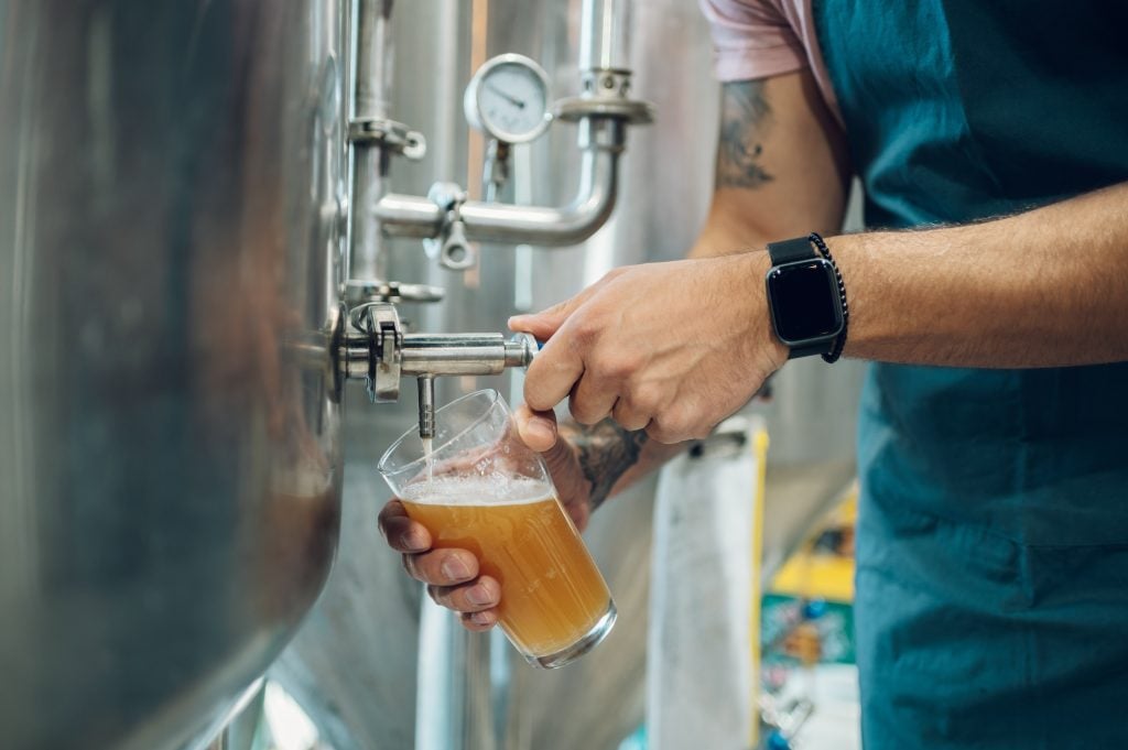 A man pouring a beer from a big steel tank at a brewery.