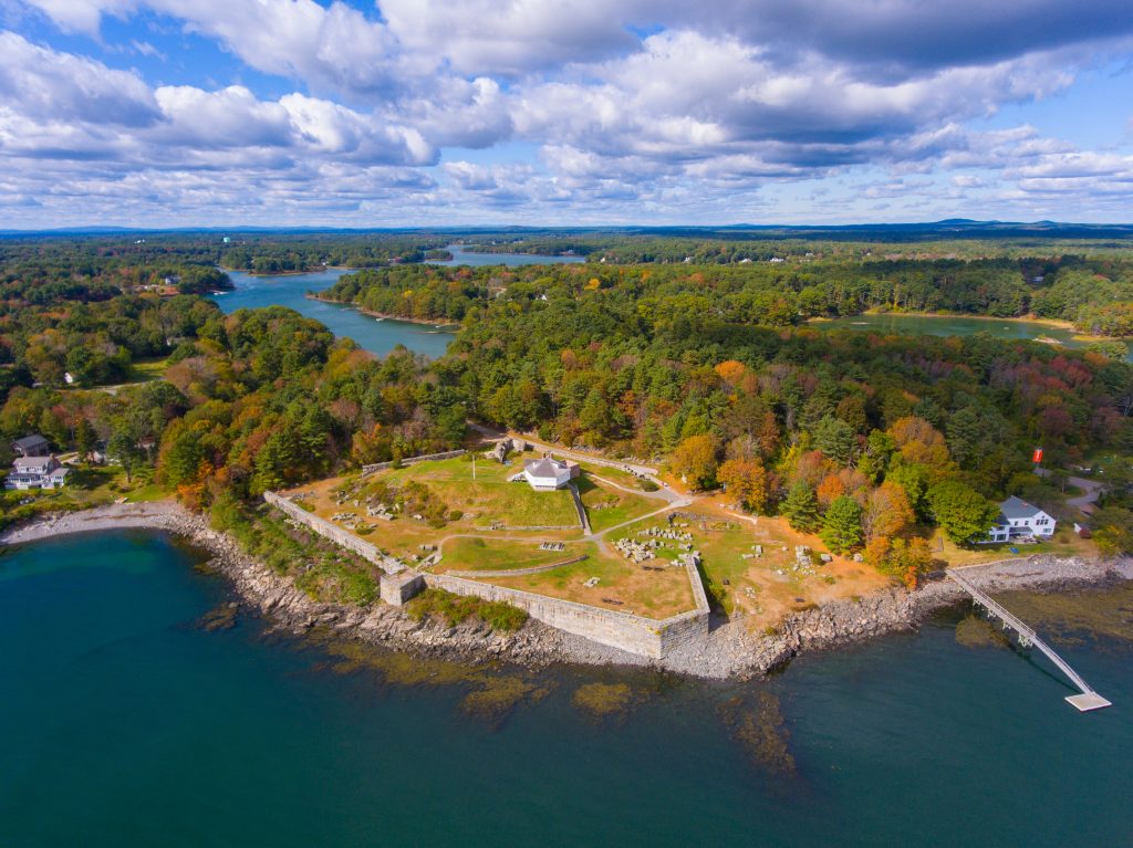 An aerial view of the Maine coastline, with a big grassy area topped with a stone fort, surrounded by stone fences.