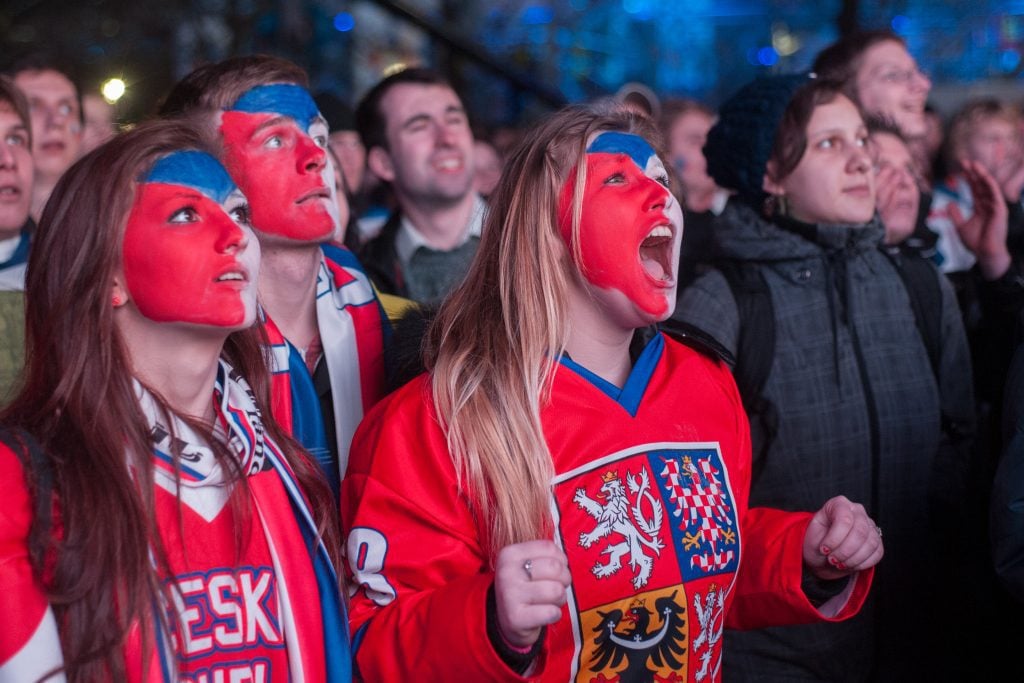 Hockey spectators wearing hockey jerseys and their faces painted red, which and blue like the Czech flag.