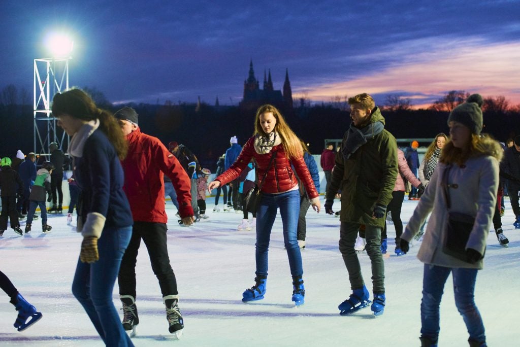 People ice skating in the evening, the outline of Prague Castle behind them.