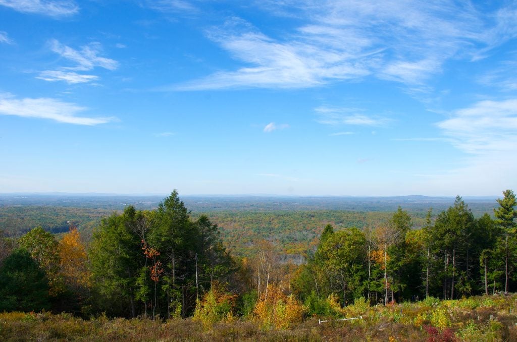 View from the top of the mountain with views of foliage-covered landscape into the distance, underneath a bright blue sky.