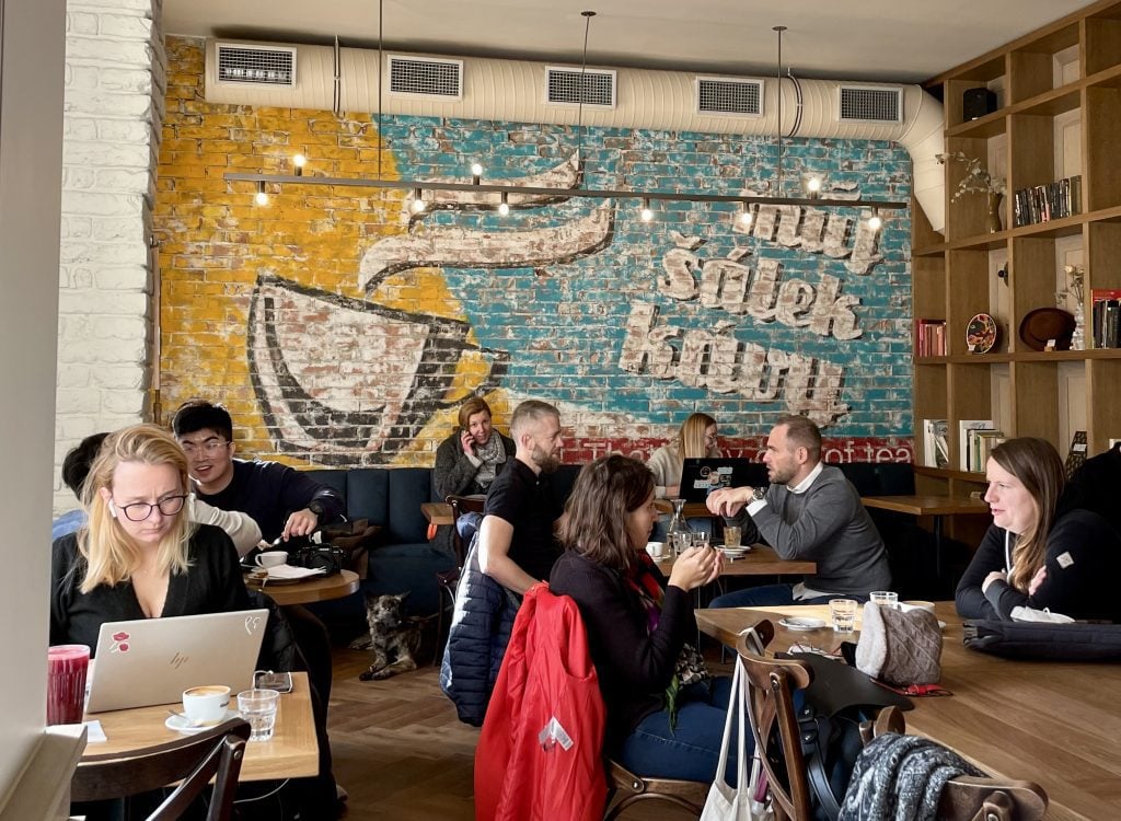 People sitting in a cozy cafe, chatting and working on laptops.