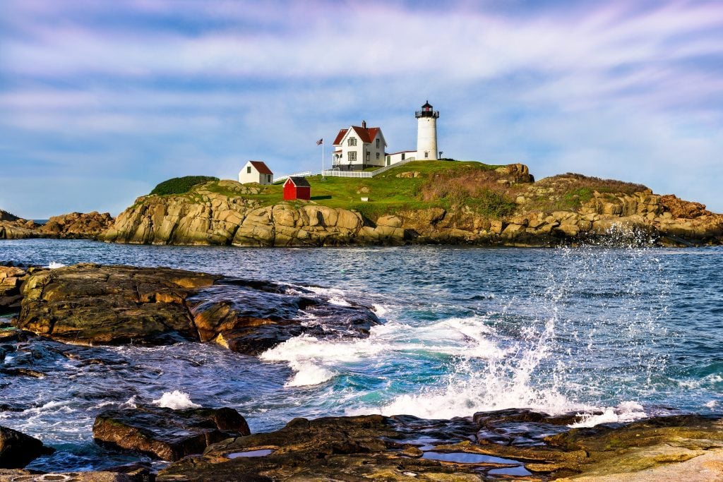 A lighthouse perched on a rocky island, surrounded by crashing waves.