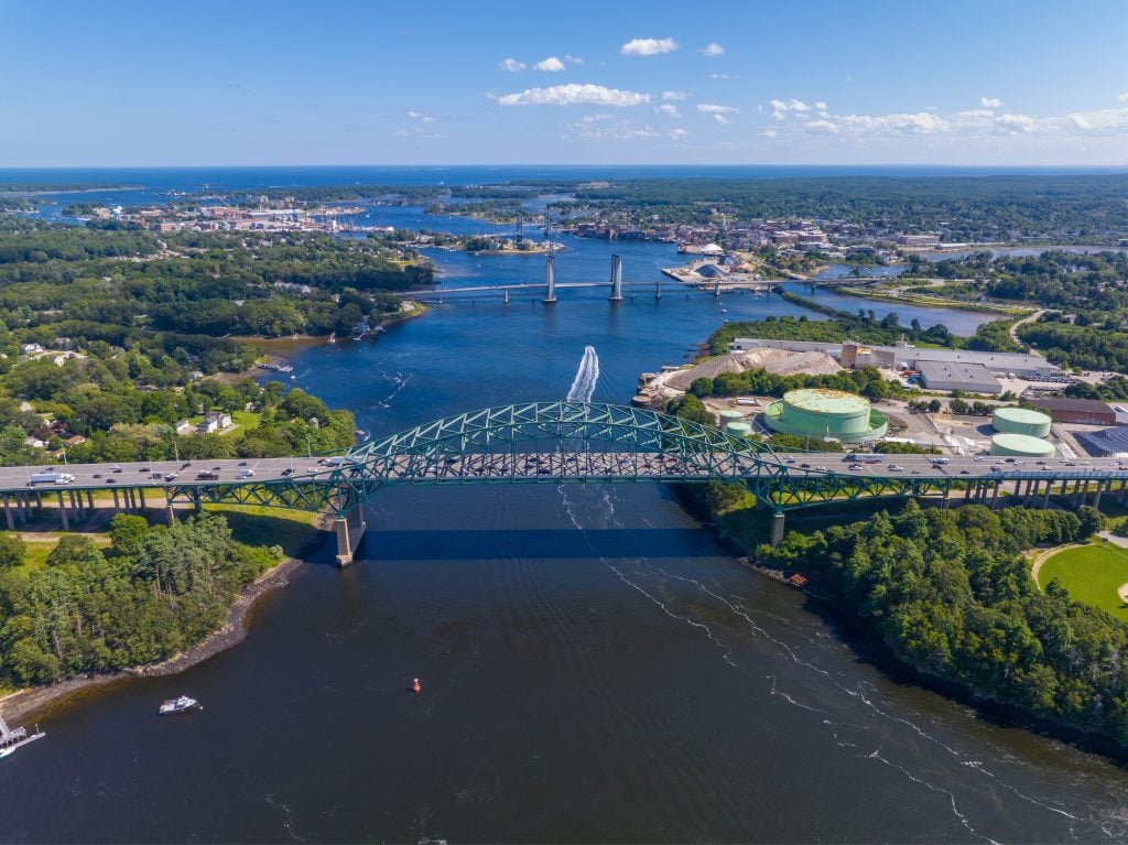 A steel suspension bridge connecting two sides of a curvy blue river.