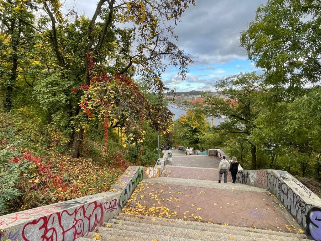 A graffiti-covered stairway through a wooded park in Prague, with some of the leaves turning red and orange.