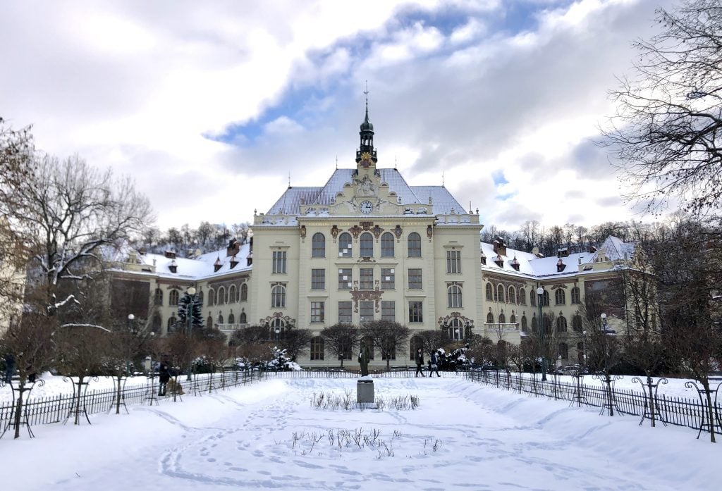 A beautifully crenellated building in Prague, set at the end of a snowy garden.