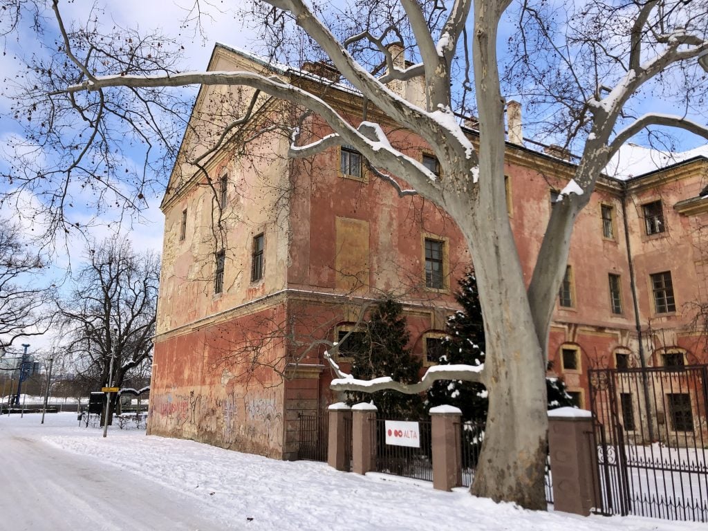 A faded red brick building in the snow on a sunny day in Prague.