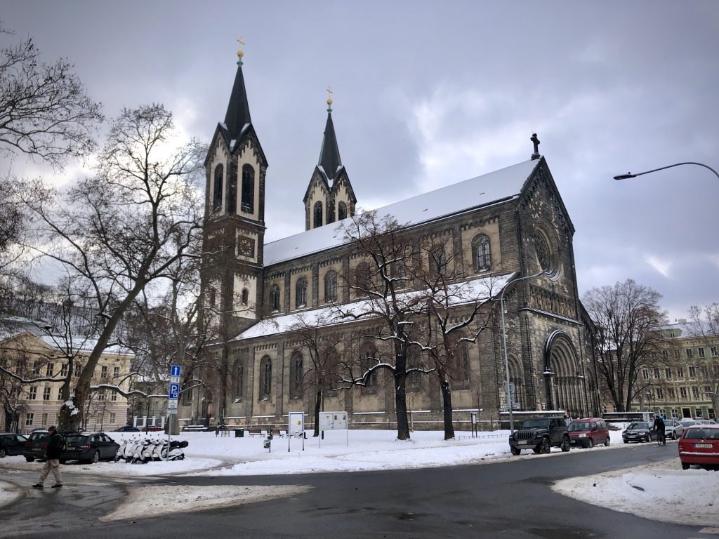 A gothic church in Prague, underneath a light layer of snow, the sky gray and dark and cloudy.