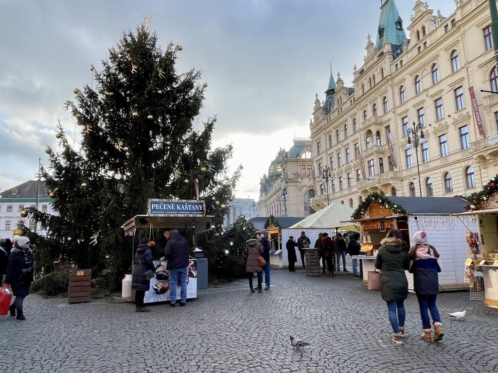 People walking past a Christmas tree and market stands in Prague.