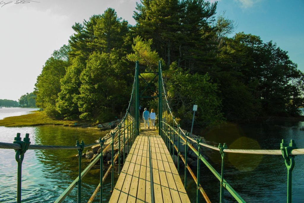 A couple walking along a narrow, wooden-plank suspension bridge.