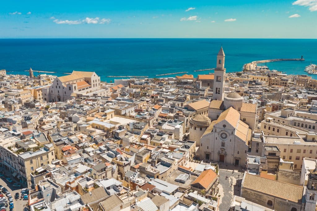 Vue aérienne de Bari, avec ses églises et ses bâtiments en pierre blanche, sur fond de mer d'un bleu éclatant.